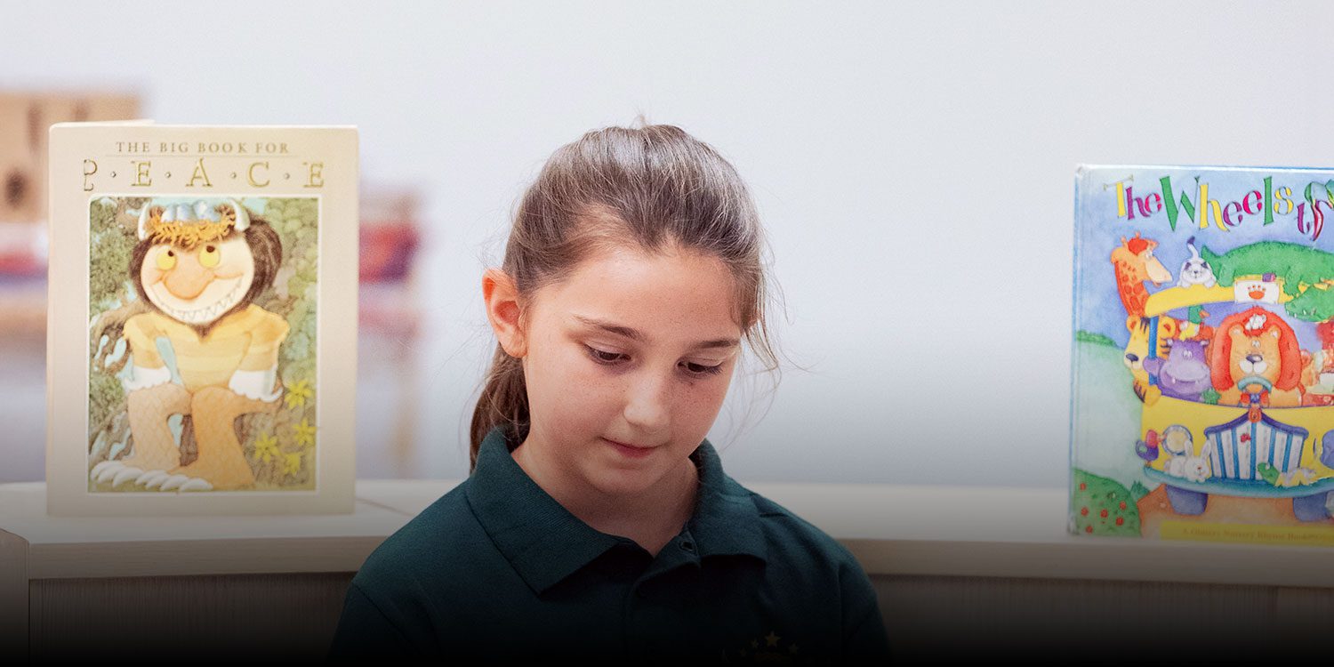 Student in a green school polo standing between picture books on a library shelf.